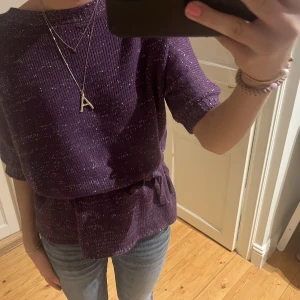 Kortärmad stickad  - Stickad lilaglittrig tröja. Antingen kan man ha den med ett band som kommer till runt midjan eller utan som på bild två. Vet tyvärr inte vart den kommer ifrån, men så cool o unik!