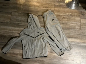 Nike Tech fleece 158-174 - Snygg Nike dress. Jackan är i nyskick. Byxorna i bra skick men finns hål i linningen, se bild. Går att sy igen. Syns inte om man har jackan till.   Finns i Handen. Kan skickas mot kostnad.