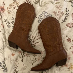 Cowboyboots 🤎 - Bruna cowboyboots. Perfekta oavsett årstid. Stl 39. Färgen ser inte helt rätt ut på kamera. Så be gärna om fler bilder så ska jag försöka för bättre ljus. Lite trasigt framme på tån som syns på bild nr 2 och ganska slitna på hälar, se bild 3. Prisförslag?