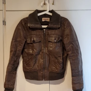 Jacka - Brun jacka med muddar. Har en liten reva i ryggen och en reva i sömmen på ärmen som går att sy ihop igen. 