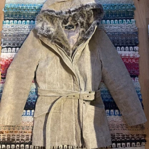Läderjacka med pälsluva - Vintage läderjacka med pälsluva! Knäpps med dragkedja och dras åt med bälte i midjan! Märkt som strl 40, skulle uppskatta som en M!