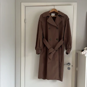 Brun Trenchcoat  - Trenchcoat från H&M med puffärmar. Stor i storleken, oversize model. Storlek XS. Använd 2-3 gånger.