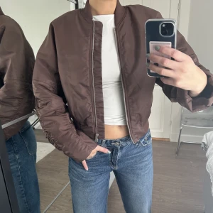 Bomberjacka  - Brun croppad bomberjacka från Gina Tricot! Använd 2 gånger och köpt för 300kr. Storlek S och jag är 173cm så är säkert lite längre på någon kortare! 
