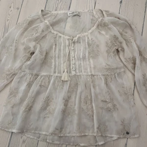 Blus - En blus från abercrombie & fitch som är beige/off white med gulddetaljer. Den är genomskinlig och är i lite mesh likande tyg. Storlek xs
