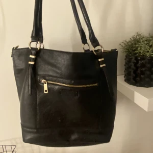 Väska - En svart väska med guld dragkedja, som jag använt 4 gånger ungefär. Jag säljer nu den eftersom den inte kommer till användning 🌸 det har gått sönder lite på framsidan (det jag tog kort på). 