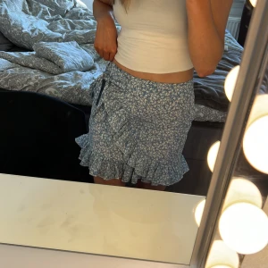 Blåvit blommig kjol  - Superfin blåvit blommig kjol med en volang och knyte. Storlek S