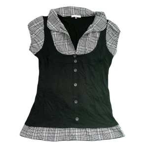 Rutig topp med svart västdetalj - Jättesöt rutig topp med krage och en svart västliknande detalj. Går att knyta där bak för en riktigt fin åtsittande passform. Bra skick, inga defekter.