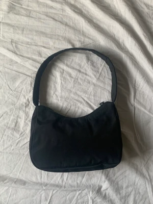 Svart axelremsväska  - Söt minibag köpt på Gina Tricot för 249 kr. Mycket bra skick 🌑 (Mynt med för uppskattning av storlek). Väskan rymmer din mobil, korthållare, smink och har även ett mindre fack för småsaker. Materialet är mjukt och inte styvt.