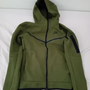Grön Nike Tech Fleece - Olivgrön Nike Tech i storlek XS. Väldigt bra skick förutom en svart prick (bild 2). PRIS KAN DISKUTERAS!