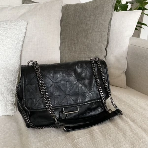 Handväska, Zara  - Svart handväska från Zara i superfint skick! Den har två öppna fack samt ett med dragkedja, ca 25cm bred. Magnetlås samt handtag och detalj i kedjor. Handtaget går att ha långt (crossbody) eller kortare som en axelväska och detaljen går att knäppa bort