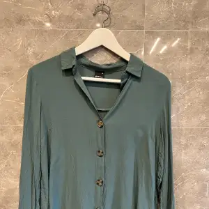 En grön skjorta/blus i storlek 36. Fina melerade knappar. 