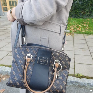 GUESS HANDVÄSKA. NYSKICK. - GUESS handväska för dam i nyskick. Kan bäras i handen eller över axeln. GUESS-påse tillkommer med väskan