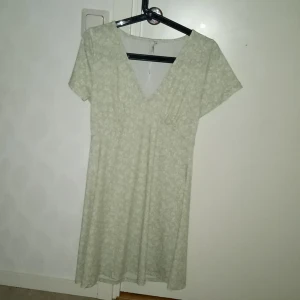 Mintgrön klänning - Säljer denna klänning med v-ring, den är ljusgrön med vitt blomtryck, den har inte blivit andvända så mkt och är därför i bra skick🙂