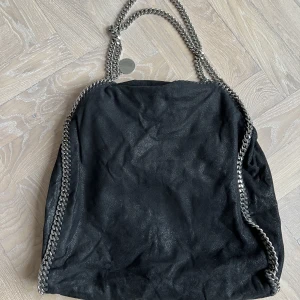 Stella McCartney svart kedjeväska - ÄKTA Säljer min Stella McCartney Svart Faux-Läder tote väska pga flytt.   Detaljer: färg: svart material: konstläder handtag på ovansidan knappfästning  en graverad logotypberlock Dustbag ingår   Väldigt fint skick.  