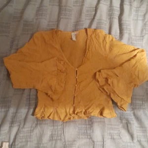 Orange volangtopp - Varan är runt 40 lång, ärmarna är runt 50 cm. Tröjan är i ett bra skick, inga defekter förekommer. 