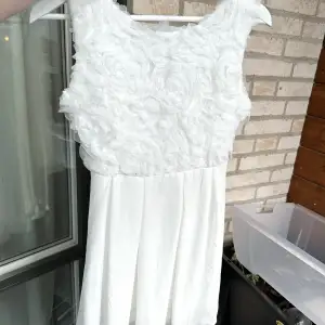 Säljer en vit klänning med ”ros” mönster upptill, samt två lager av tyg nertill. Klänningen är inte genomskinlig.  Klänningen slutar ungefär lite över knäna på mig (156cm).  Klänningen är endast använd en gång på dop. Så de är i ett mycket fint skick.