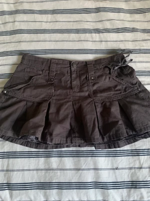 Lågmidjad kjol - Säljer nu denna gulliga lågmidjade kjolen. Den har ett siden aktigt material på insidan och detaljer som små nitar. Även ett litet band vid ena sidan för att kunna spänna i midjan. Tvärs över är det ca 40 cm i midjan. Skriv vid funderingar💞