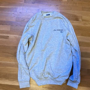 Hoodie - Sweatshirt ljusgrå med texten ”club athletic” i mörkblå. Bra skick 
