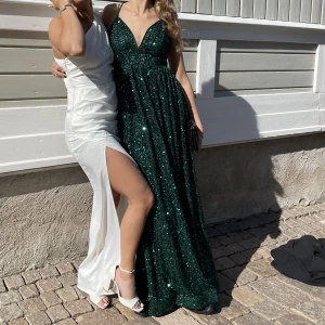Balklänning - Jättefin smaragdgrön balklänning med paljetter och knytdetalj i ryggen. Är i nyskick då den endast använts en gång.  Storlek M men jag som normalt har S passade perfekt i den då knytningen gör att storleken går att anpassa för S-L. Köparen står för frakt