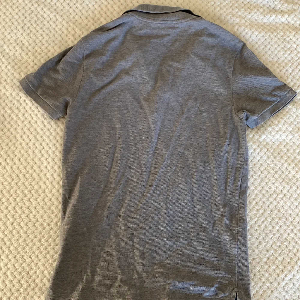 Grå Lacoste pikétröja i vädkigt bra skick, har använt den ett fåtal gånger. Den här slimfit, alltså sitter rätt tajt och är i modellen xs.. T-shirts.