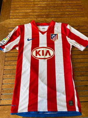 Atletico Madrid fotbollströja (retro) - Detta är Atletico Madrids hemmatröja ifrån säsongen 08/09. Under denna säsongen spelade legenden Kun Aguero i den randiga tröjan.  Skick: 8/10 ( finns någon fläck men som inte är så synlig)  Mått: nacke till mudd: 74 cm, armhåla-armhåla 48 cm