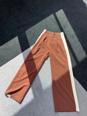 Byxor - Coola highwaist bruna byxor med vit rand i ytterbenet från Stradivarus. Sparsamt använd och i nyskick. 