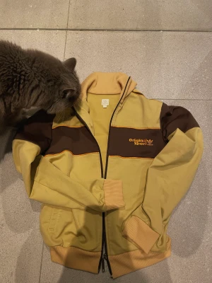 Retro 70-tal adidas jacka - Cool vintage adidas jacka i fina höstiga färger, jackan är beige/brun och inte lika gul i verkligheten som på bilden. dragkedjan är trasig på ena sidan så den kan vara lite jobbig att stänga ibland annars är den i väldigt fint skick 🫶🏼STORLEK 38