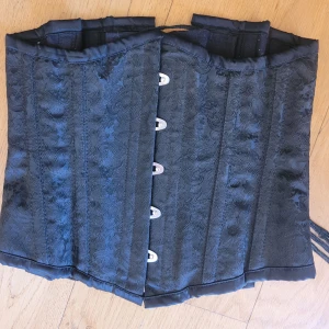 Äkta korsett från Burleska st 24 - Äkta underbust korsett från Burleska i storlek 24. Den har stålskenor och kan dra in midjan ordentligt. Med rygglapp. Vackert subtilt mönster. :) 