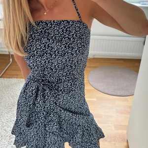 Sommarklänning! - Säljer finaste marinblåa sommarklänningen med vita blommor på!! 😍Använd fåtal gånger så den är som ny. Klänningen är omlott med knytning i sidan. Hör av er om ni har några frågor ❤️