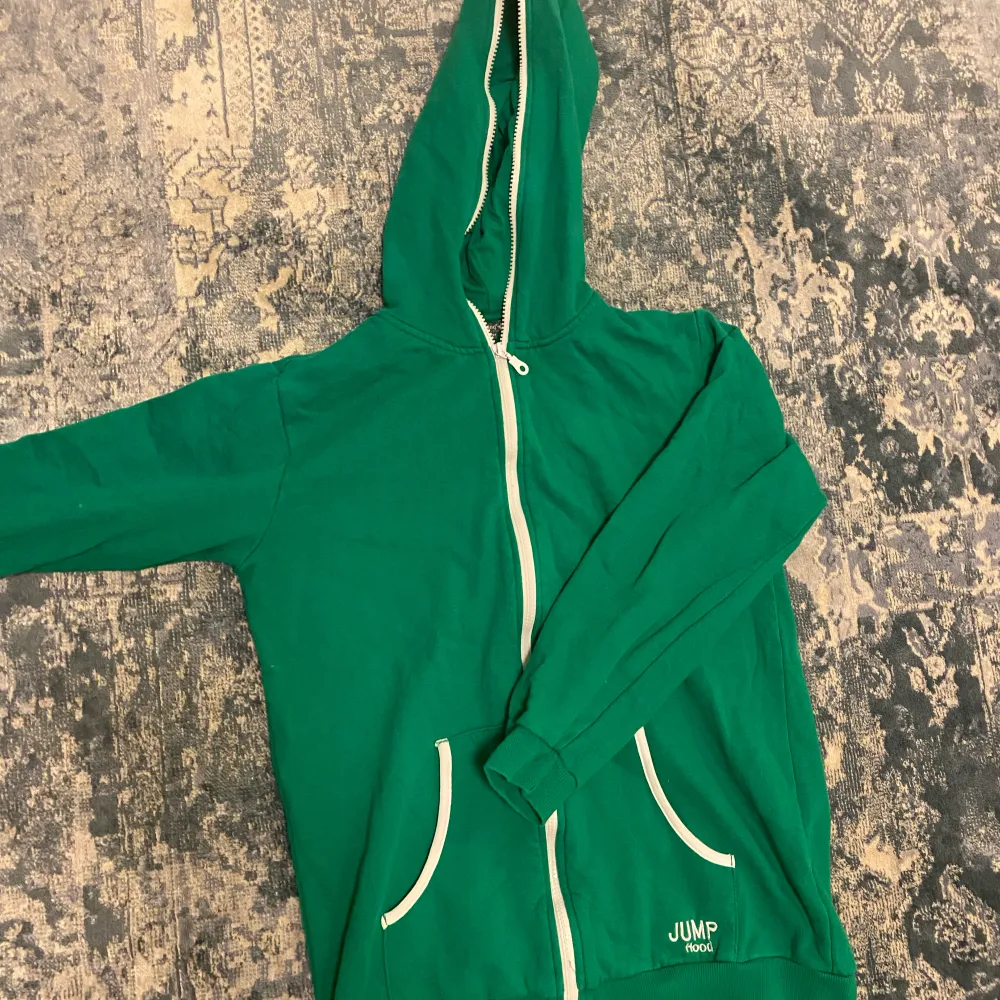 En grön zip up hoodie med vita detaljer, lite kortare model i armarna. Hoodies.