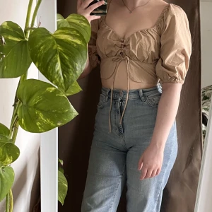 Topp med snörning 🥯 - Beige croptop med snörning. Ballongärmar, resår i rygg. Använd endast en gång. 📦