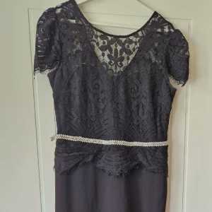 Svart balklänning  - Svart balklänning säljes. Svart topp i spets, korta holkärmar, fastsytt glitterbälte i midjan. Elastisk figursydd långkjol formar sig längs kroppen höfter och utställd. Storlek UK 12, motsvarande 40/42 i Sverige. Lång i kjolen funkar med klack/lång person