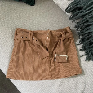 brun kjol - En brun kjol med skärp-spänne! Går ner till nedre delen av låren på mig som är 153. Manchester mönster. Aldrig använd.