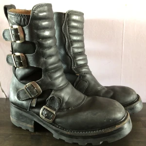Buffalo Biker Boots stl 42 - Säljer mina stentunga (bokstavligt talat) boots från Buffalo. Äkta, tjockt läder i begagnat men fint skick. Ett spänne trasigt på vänster sko, punkigt fixat med en säkerhetsnål. Tjock sula helt i gummi, väger SATAN, skickar därför ej. Fler bilder i Pm!!