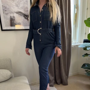 Denim jumpsuit - Jumpsuit gjord av tunt denim i mörkblå tvätt. Den har rak passform och ankellånga byxben. Endast använd en gång då den är lite för liten för mig.