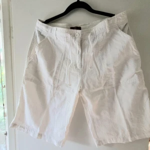 Vita Linneshorts - Snygga vita shorts i linne. Fickor fram och bak. Skulle säga stl.M : 85cm i midjan runt om, innerbenslängd ca 26cm. Seconhandfynd! 