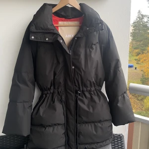 Varm vinterjacka  - Varm vinterjacka som aldrig har används. Inbyggd luva som du kan gömma eller ta fram. Snörning för att markera midjan. Rosa orange färg inne i jackan. Storlek S men är oversized så passar absolut en M. Ordinarie pris 1599:-🧡skriv för fler bilder.