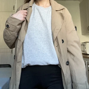 Lång beige trenchcoat - Lång beiga trenchcoat, gott skick. Storlek M. Upphämtas i centrala Handen eller Mariatorget, Södermalm. Tar betalt via swish. 