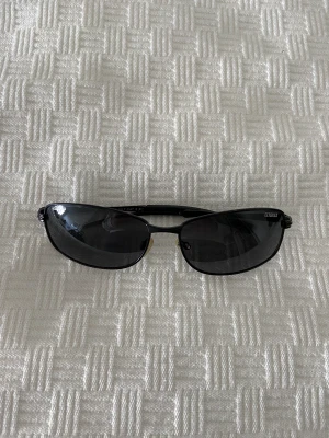 Coola 90s solglasögon  - Ett par coola 90s vintage solglasögon 🖤Lite dad vibes med tunn båge och fyrkantiga glas 😎 Ena bågen har tappat lite plast, med det påverkar inte användandet alls! Annars hela och fräscha! 