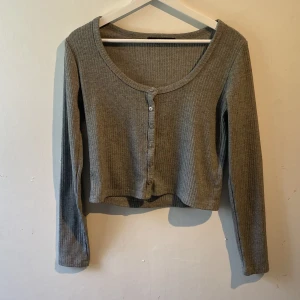 Kofta  - Grå kofta/topp? Den har knappar på framsidan och den är uringad och ribbad st L men sitter som M
