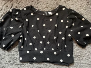 Topp - En svart kroppad topp med prickar på från H&M. Toppen har öppenrygg med knytning. Strl xs. Säljer pga att den är förliten (har tyvärr inte bild hur den sitter på)