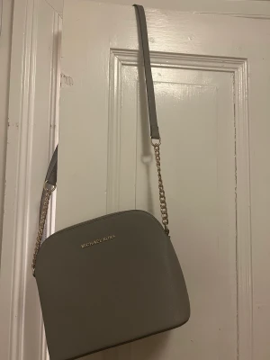 Michel kors väska - En grå Michel kors väska med guld detaljer. Lite slitningar på axelbandet men annars i bra skick!