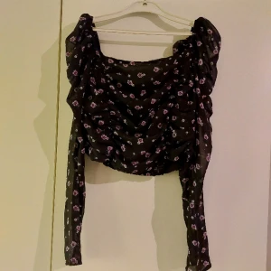 Svart blus - Svart blommig blus med lila blommor. Skönt material och stretch vid mage samt byst.
