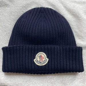 Mössa Moncler - Marinblå Moncler mössa men den traditionella loggan i nyskick. Köpt från NK i Göteborg, använd 1-2 gånger. Pris kan diskuteras vid snabb affär.