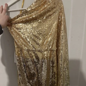 Klänning  - Guldig paljettklänning från NA-KD. Aldrig använd och har kvar lapparna. 