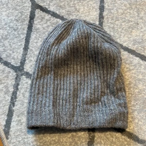 Grå stickad mössa  - Stickad mössa i mjukt tyg aldrig använd! Passar normaltstort huvud och är stretchig