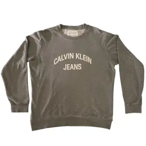 Snygg grå crewneck tröja från Calvin Klein Jeans i fint skick.  Har inte hittat några fläckar eller något vidare synligt slitage. Strlk XL, 64cm i bredd, 72cm i längd (baksida).