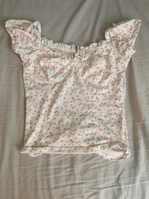 Blommig topp Nelly  - Jag säljer en vit topp med rosa blommor från Nelly i storlek M. Fint skick, endast använd ett par gånger.