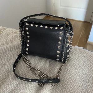 Handväska - Handväska med nitar. Ena remsan till dragkedjan har ramlat av men jag har kvar den så det går lätt att laga med lite ståltråd. Köparen står för frakten. 