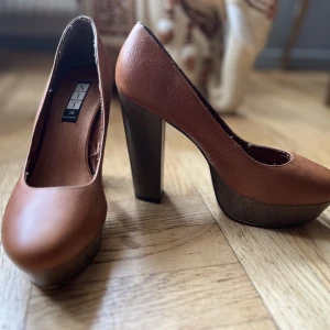 Ljusbruna pumps - Pumps i ljusbrun läder (äkta) med träklack och platå (fejkträ). Sparsamt använda med några enstaka märken på klack och platå. Storlek 38, vilket stämmer bra. 